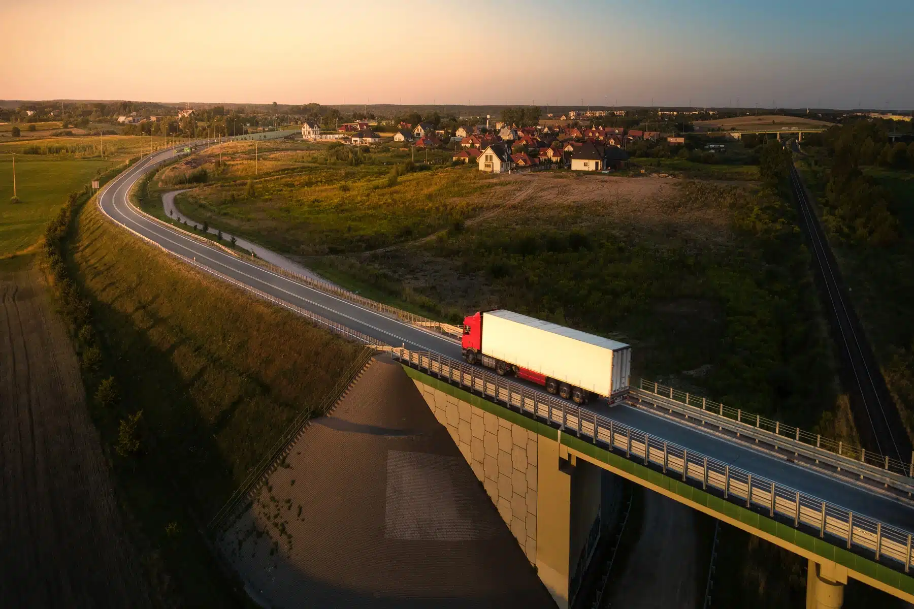 Aerial view of a truck driving along a countryside road at sunset, with a village and bridge visible in a Nordic landscape, representing a fleet running on renewable diesel