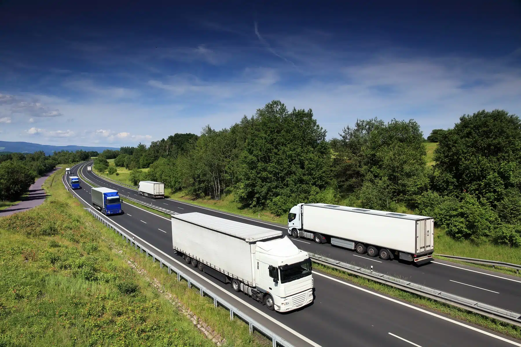 Klimaregler i transport: flere lastbiler kører på en flersporet motorvej gennem grønt bakkeland – et billede på den vejgodstransport, der er underlagt EU's klima- og emissionsregler