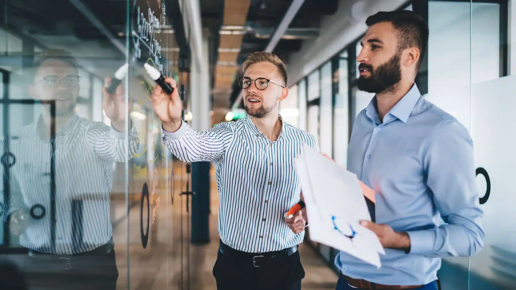 Two business professionals reviewing a compliance strategy on a glass whiteboard covered in notes and diagrams, representing the planning fleets need to navigate EU climate regulations for transport