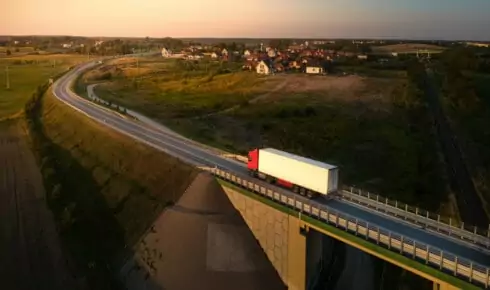 Aerial view of a truck driving along a countryside road at sunset, with a village and bridge visible in a Nordic landscape, representing a fleet running on renewable diesel