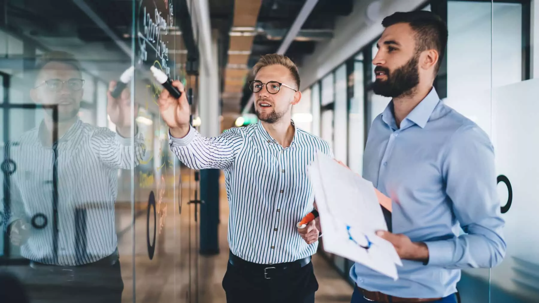 Two business professionals reviewing a compliance strategy on a glass whiteboard covered in notes and diagrams, representing the planning fleets need to navigate EU climate regulations for transport