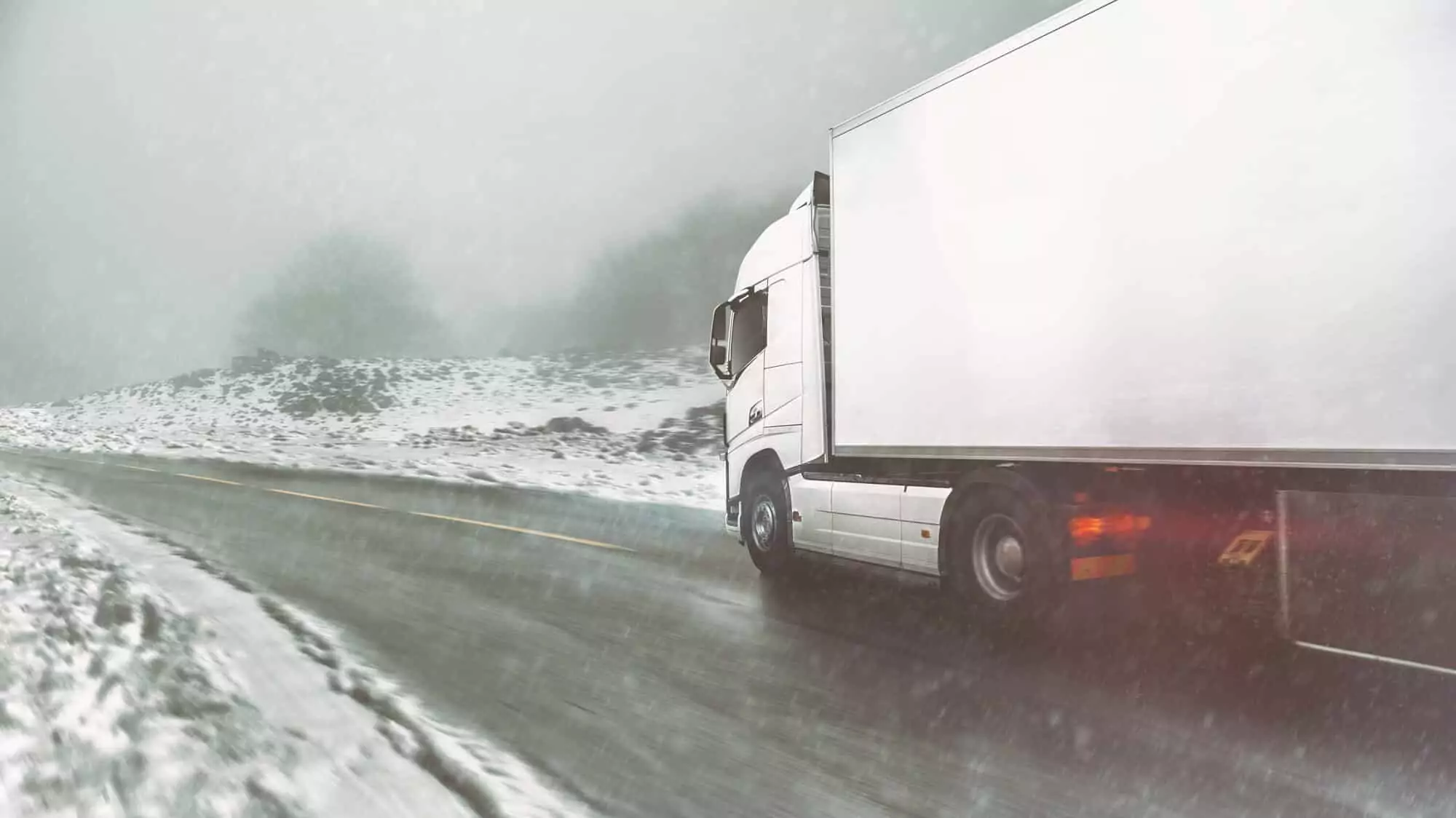 A truck driving on a snow-covered road during heavy snowfall, illustrating winter fleet operating conditions in the Nordics