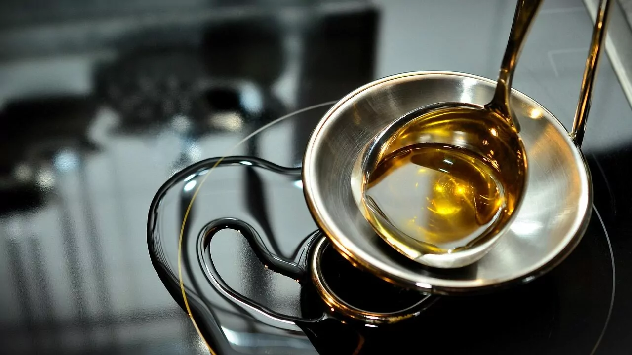 Close-up of golden oil being poured from a spoon into a small metal bowl, representing the waste-oil feedstock category used alongside rapeseed in biodiesel production
